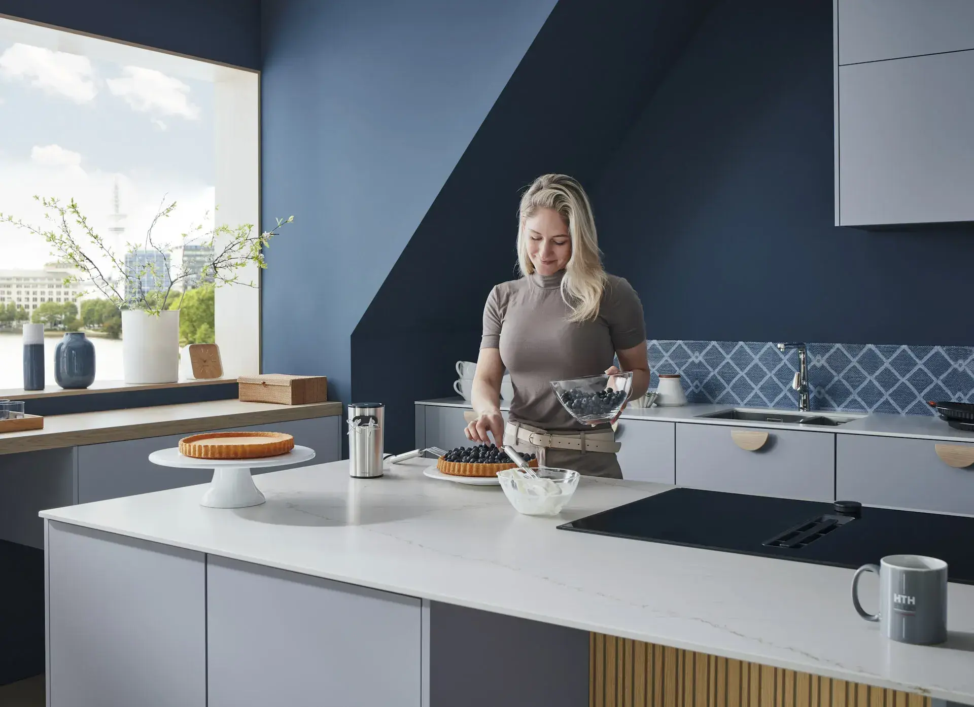 Model steht hinter der Kücheninsel mit NEFF Induktionskochfeld mit Muldenlüfter, Schublade, Mix aus Lack, Matt und Eiche